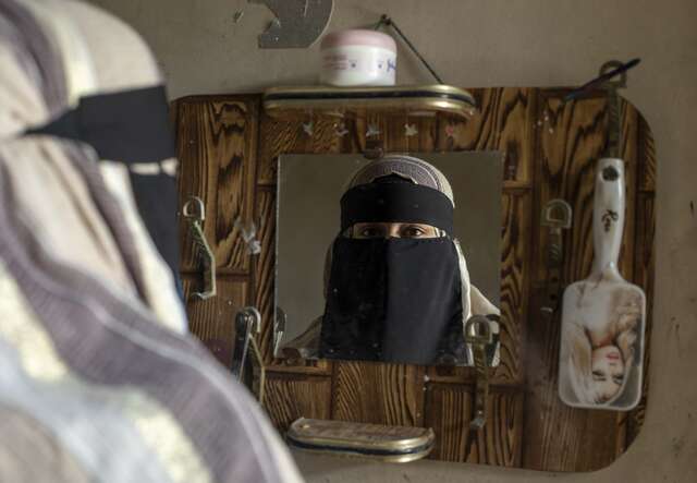 Eine Frau im Niqab spiegelt sich in einem verzierten Spiegel.